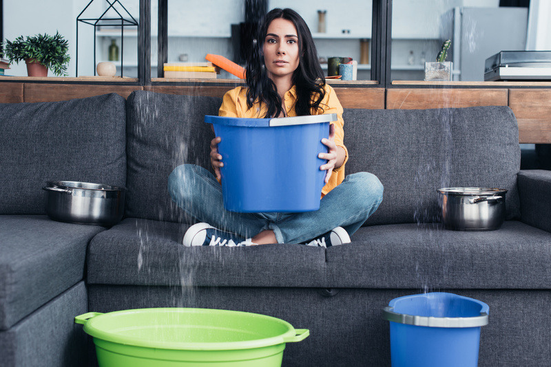 Woman sits while catching water in a bucket from her leaky roof